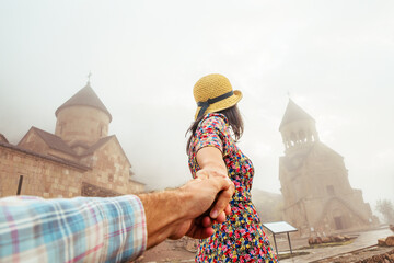 Close up millennial blogger show Follow me hold hand to the tourist attractions of Armenia. Happy woman traveler wear red summer dress at the entrance to famous Noravank monastery