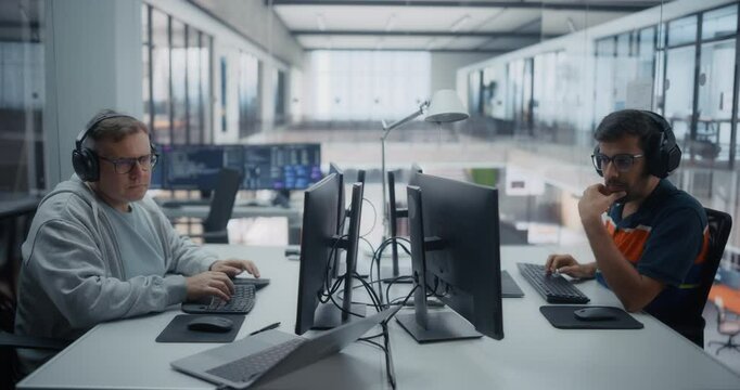 Male Programmers in Headphones Sitting Side by Side in a Glass Room, Focused on Writing Software Code. Male Colleagues Working in Office, Researching and Developing Innovative Machine Learning Methods