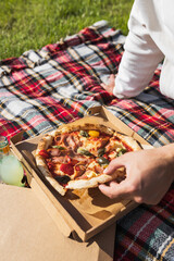 Man's hand with a piece of fresh pizza outside in picnic setting