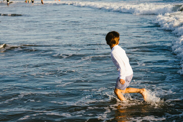 Fototapeta premium Little boy splashing in blue water happily in summer