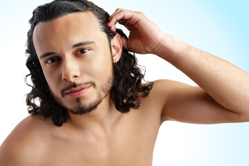 Young man with curly hair thoughtfully posing against a plain background