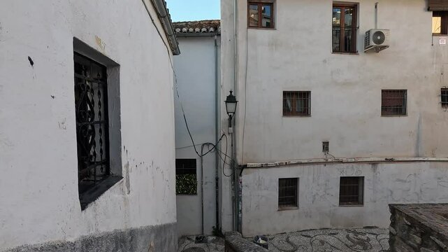 Morning light casts a golden glow over the Albaicin narrow, winding alleys. White Moorish facades bask in tranquil serenity, reflecting the historic charm of this Granada neighborhood. Granada, Spain