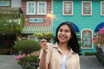 Fototapeta premium portrait of beautiful happy young asian woman holding sparklers fireworks to celebrate new year eve with garden party standing in outdoor vintage house yard