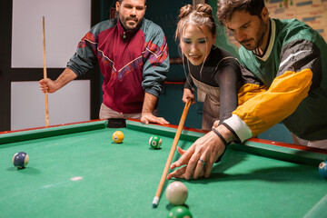 Young friends playing pool billiard game together enjoying entertaining evening activity at modern sports bar