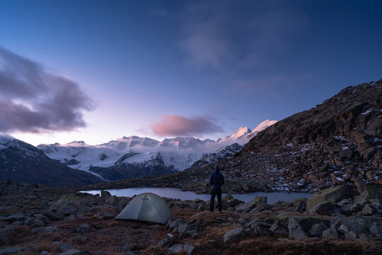 A man and his tent at a lake in the Bernina mountain group, Switserland, during dawn.