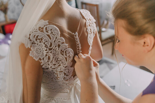 A woman is getting her wedding dress altered by another woman. The bride is wearing a white lace dress and the other woman is adjusting the dress