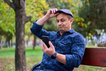 Obraz premium Mature man using cellphone on a bench in the park