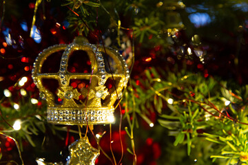 Bejewelled, regal golden crown Christmas tree decoration with bokeh and red tinsel
