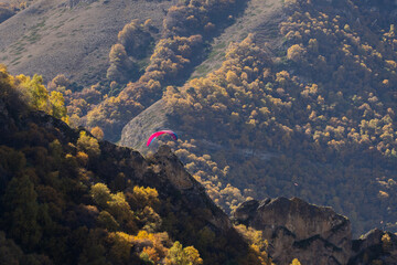 Fly Chegem paragliding site is "Mecca" for extreme sports enthusiasts. View from ground of paragliders flying against backdrop of rocky mountains of Chegem Gorge. El-Tyubu, Russia - October 7, 2024