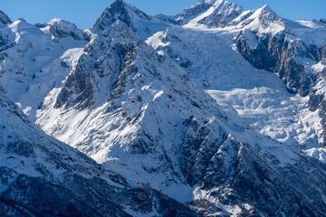 Snowy peaks and glaciers cover giant rocks. Pine and spruce forests grow at foot of mountains. which Majestic mountains against blue sky. Sunny day. Autumn 2024. Karachay-Cherkessia. Dombay.