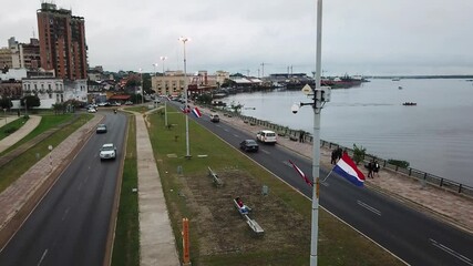 Paraguayan flag waving in the wind on costanera avenue, with the paraguay river and the city of asuncion in the background