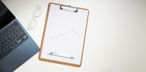 Top view of office workplace table with charts report on wooden clipboard, glasses and pen.