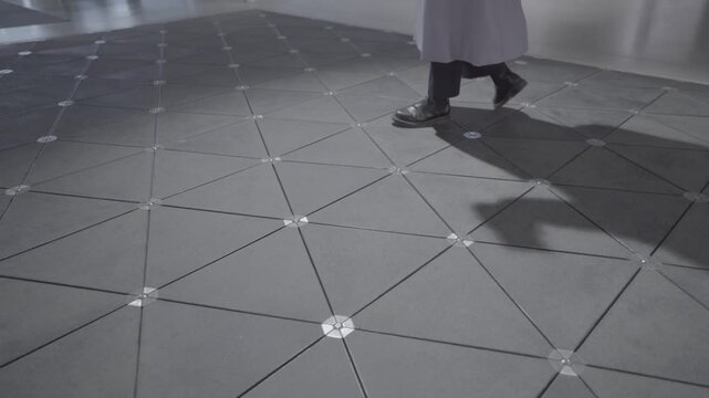Cesis, Latvia - November 13, 2024 - Person walking on a high-tech geometric floor with triangular tiles, designed to generate electricity from footsteps.
