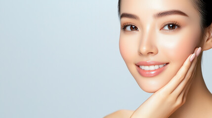 Fototapeta premium Radiant young woman showcasing healthy skin, smiling gently while touching her face against a soft, light background