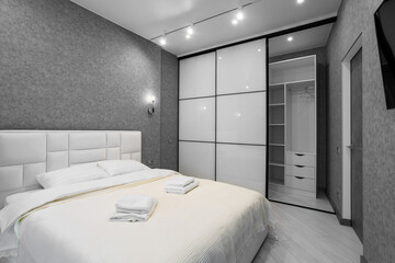 A well-appointed small modern bedroom with a cozy design, featuring a queen-sized bed, bedside tables. A large window with curtains allowing soft daylight.