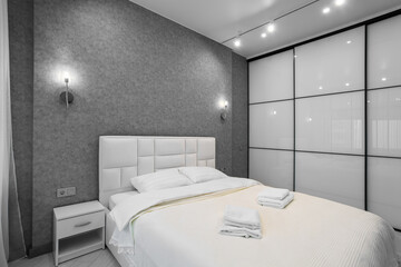 A well-appointed small modern bedroom with a cozy design, featuring a queen-sized bed, bedside tables. A large window with curtains allowing soft daylight.