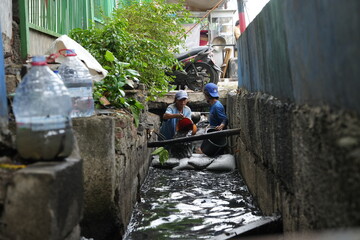 a group of men cleaning the gutter sewage water draining out from cement drain pipe into the...