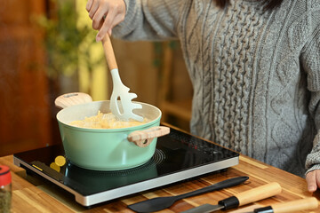Cropped shot woman stirring pasta in a green pot, preparing a meal during the holidays