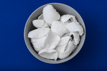 Miseczka przekąsek, solone prażynki ziemniaczane na niebieskim intensywnym tle 