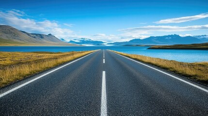 Naklejka premium Empty road leading to a lake and mountains under blue sky.