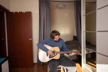 Man Practicing Guitar in Cozy Bedroom, person enjoying music as a hobby,