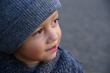 close-up photo of a little boy with brown eyes in a gray hat on a gray background