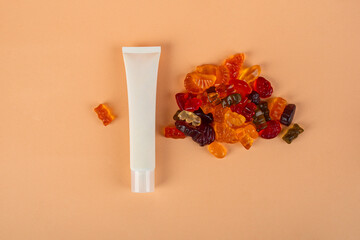 Cosmetic product in tube, bottle, lotion or serum and colorful candies, jelly on cream background. 