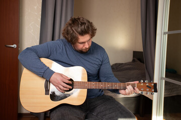 Obraz premium Man Practicing Guitar in Cozy Bedroom, dedicated performer enhancing musical skill, focus on teaching himself through study.