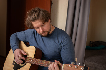 Man Playing Acoustic Guitar Indoors, studying chord, learning music, practicing for performance,...
