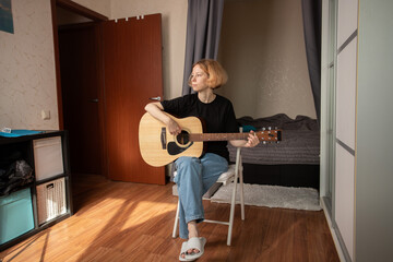 Woman playing acoustic guitar at home, aspiring musician mastering performance skills,...