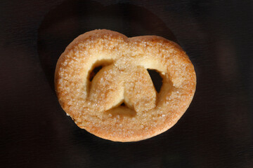 A pretzel-shaped cookie sprinkled with coarse sugar on a dark background