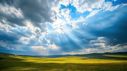 Obraz premium Expansive Landscape with Sunlight Breaking Through Dark Clouds Over Rolling Green Hills and Clear Blue Sky in a Serene Natural Setting