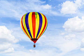 Colorful hot air balloon flying over blue sky with white clouds	