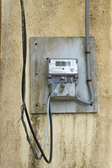 Close-up of an old electric meter mounted on a wall with wires running down the side.