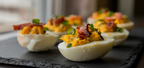  deviled eggs topped with crispy bacon and green onion, creating a savory and colorful appetizer....
