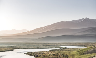 High mountain landscape panorama, a river in the mountains flows in a mountain valley among green meadows against the backdrop of mountains, landscape in the Pamir Mountains for background