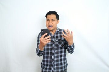 furious asian man screaming holding smartphone with angry face wearing casual shirt isolated on white background