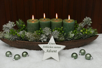 Vierter Advent: Adventskranz mit grünen Kerzen und Adventschmuck im Schnee.
