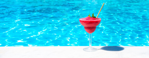 Vibrant red frozen drink with mint garnish on poolside edge in sunny weather. Concept of refreshing...