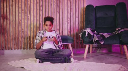 An excited African American boy plays his favorite video game at night, using a joystick and basking in the neon glow, celebrating his gaming success.