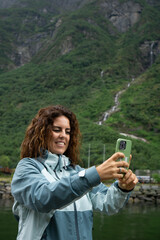 Close-up of a brunette woman in her 30s taking a photo with her smartphone surrounded by the nature of a Norwegian fjordportrait,