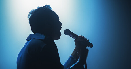 Portrait of a Handsome Young Man Singing a Song at a Music Contest. Cinematic Spotlight Creates a Silhouette Effect, His Charismatic Stage Presence and Lyrics Electrify the Stage