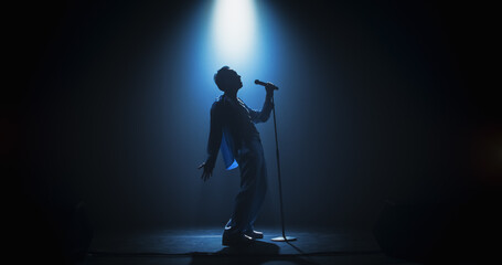 Portrait of a Handsome Young Man Singing a Song at a Music Contest. Cinematic Spotlight Creates a Silhouette Effect, His Charismatic Stage Presence and Lyrics Electrify the Stage