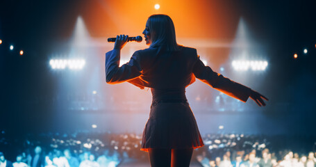 Energetic Pop Artist Performing on Stage in Pink Feminine Clothes. Excited Audience Listening to...