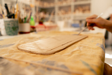 close-up in a modeling studio, female hands cut out the desired shape on clay plate, blank, ruler and wooden stack