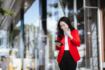 Beautiful Asian businesswoman walking confidently on a modern city street, smiling while using a smartphone. Success, urban lifestyle and modern communication.