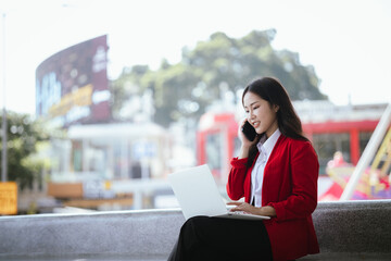 Fototapeta premium Asian businesswoman in red suit holding tablet while standing in city during daytime