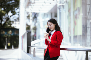 Stylish Asian businesswoman standing confidently in an urban setting holding a tablet. She is dressed in a professional business suit, demonstrating modern leadership and corporate success.