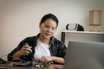 A woman is sitting at a desk with a laptop and a toolbox. She is wearing safety glasses and she is working on a project