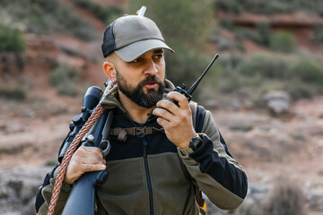 Fototapeta premium Hunter using walkie talkie carrying rifle in forest